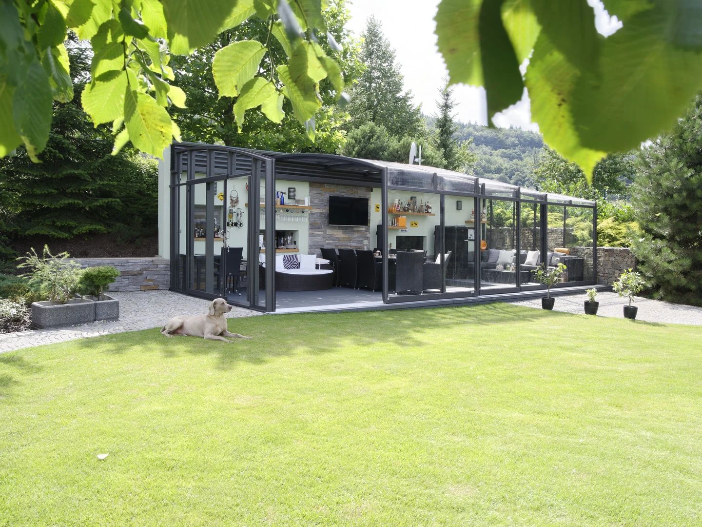 Glass garden room with the walls slid open, bar and seating inside and a dog on the lawn (supplier photograph)