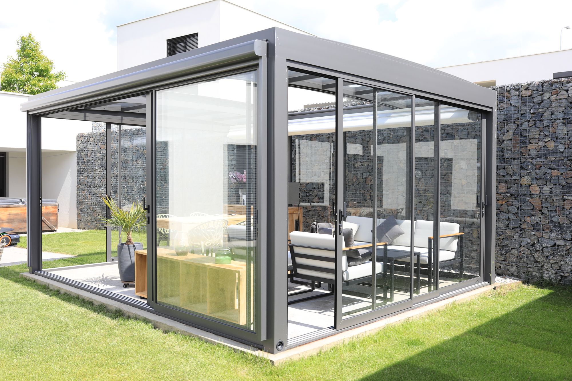 A finished glass garden room on a lawn, set against a stone gabion wall
