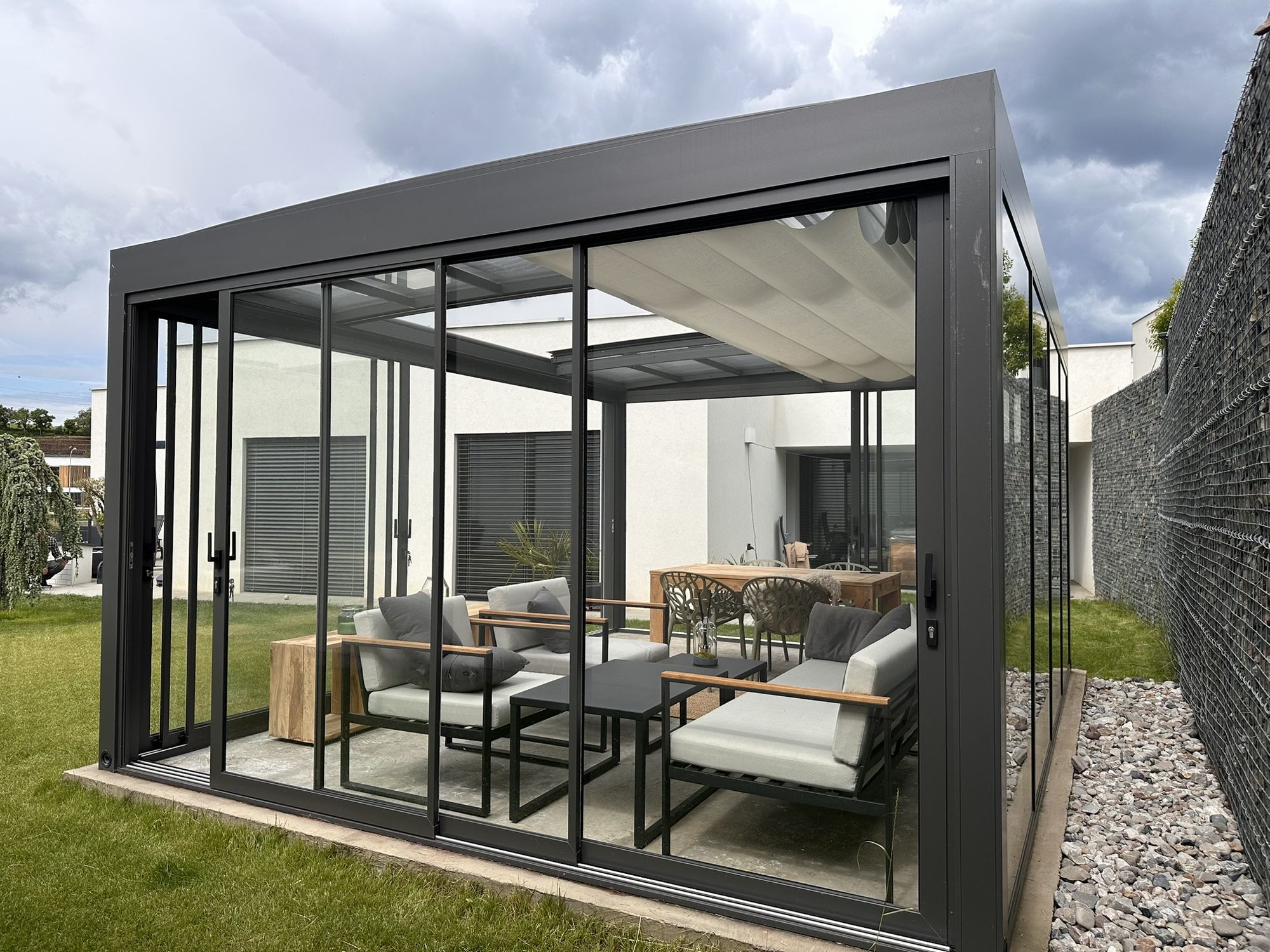 A glass room on a lawn with two of its glass walls slid back, the seating open to the garden