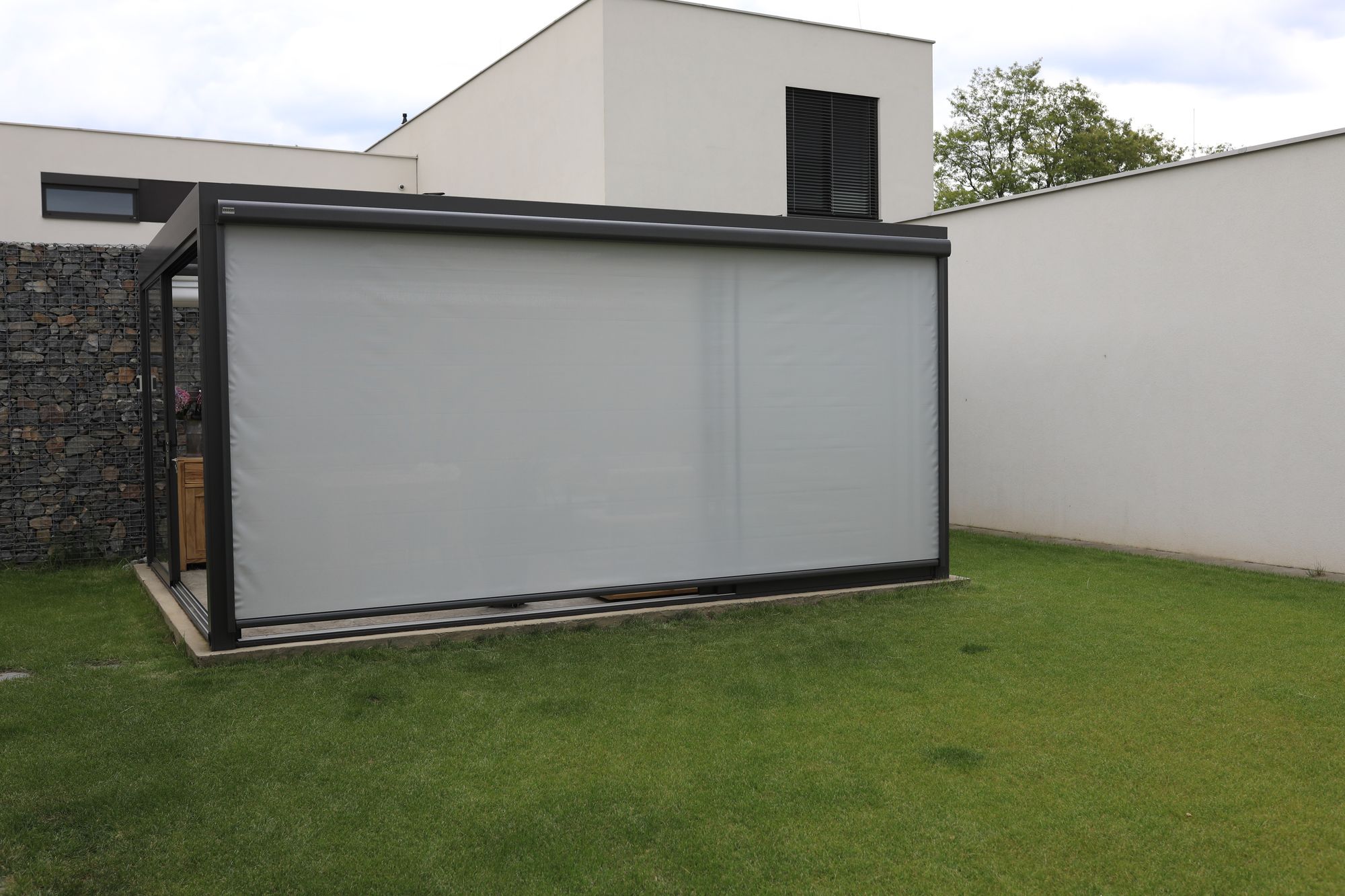 A glass room with its side screens lowered, seen from the lawn